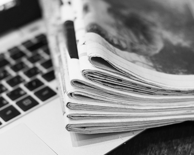 Newspapers and laptop. Pile of daily papers with news on the computer. Pages with headlines, articles folded and stacked on keypad of electronic device. Modern gadget and old journals, focus on paper